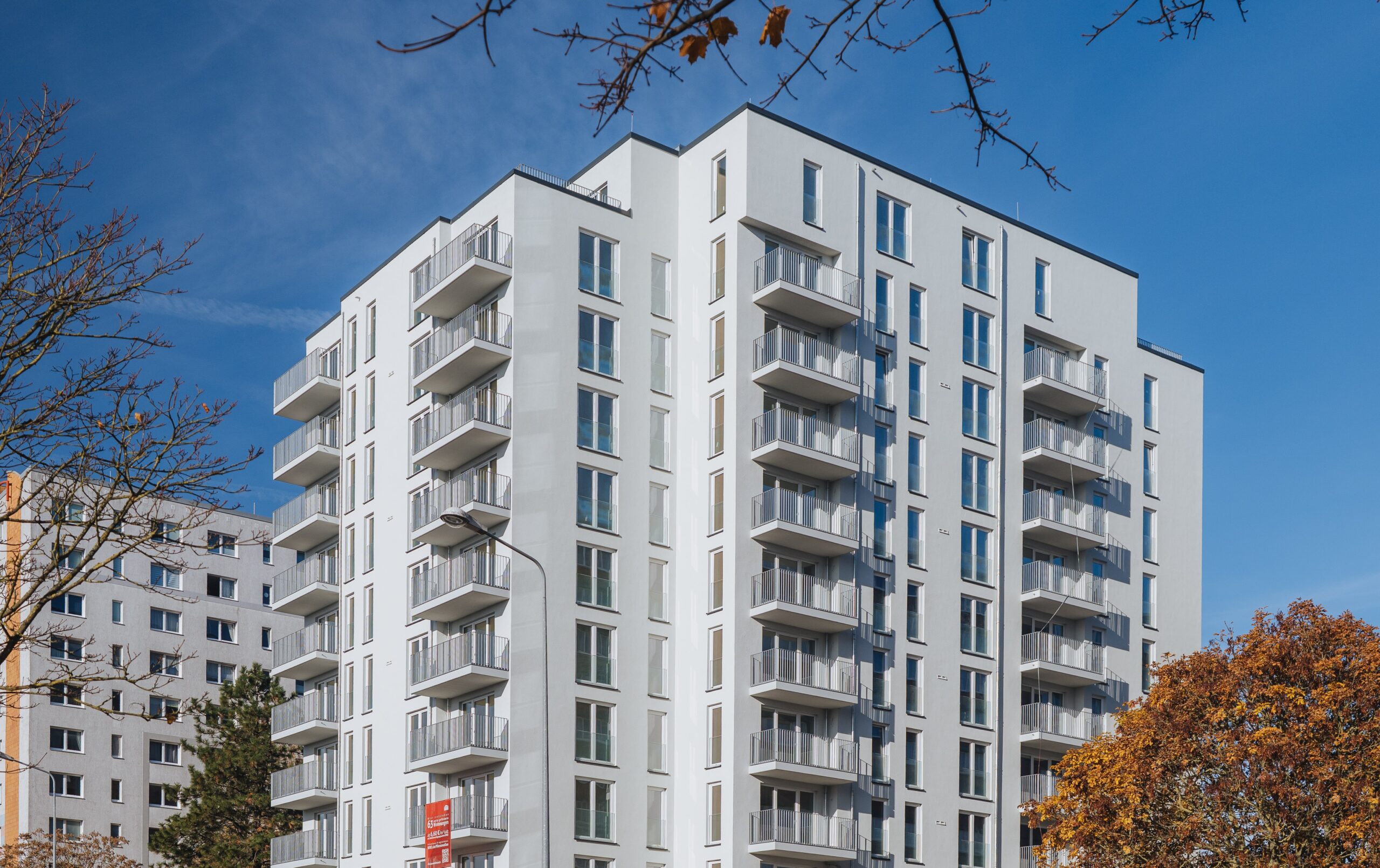 Außenansicht eines modernen mehrgeschossigen Wohnhauses mit Balkonen, großen Fenstern und begrüntem Umfeld.