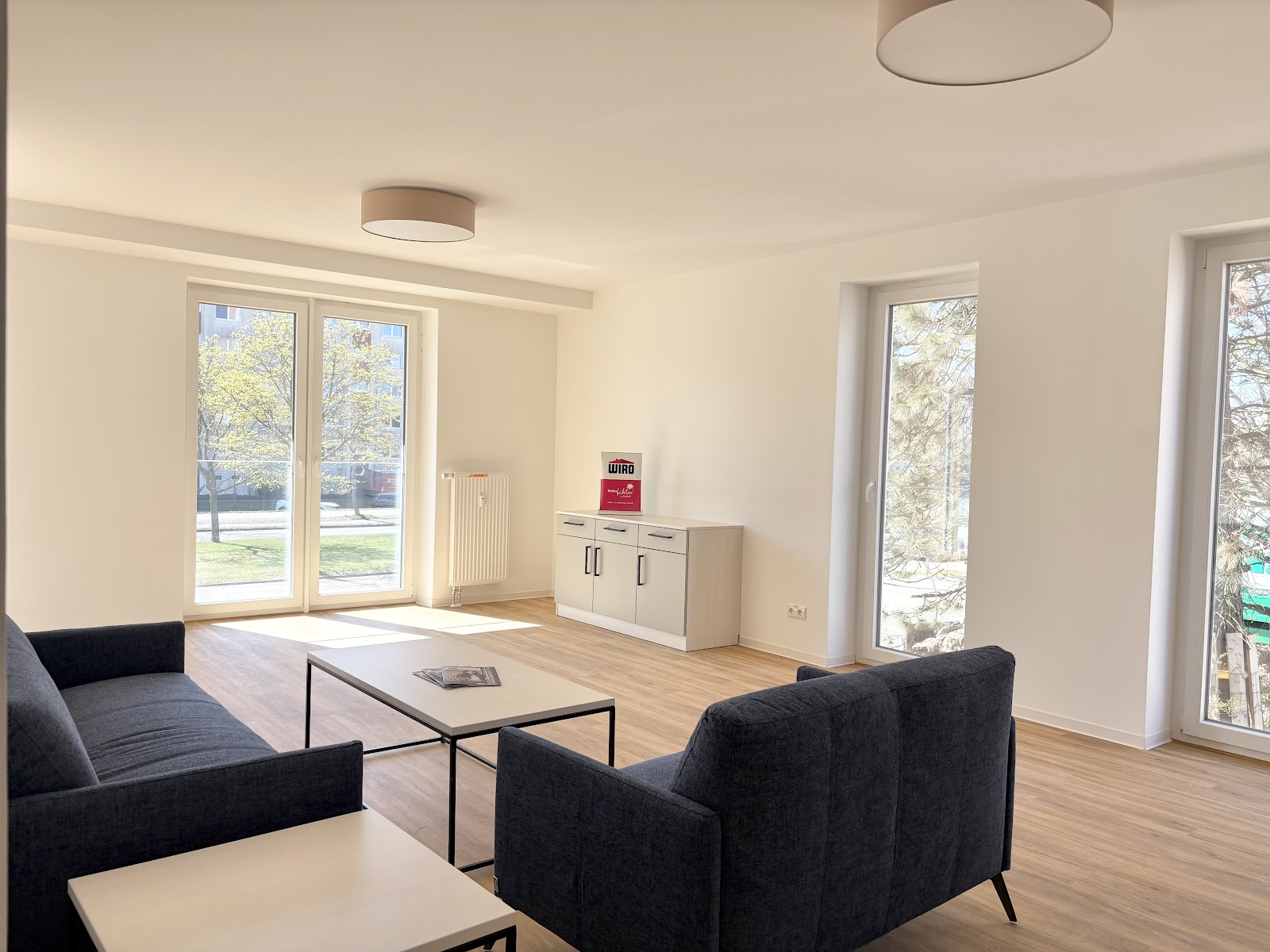 Heller Gemeinschaftsraum mit Sofas, Couchtisch, Schrank und großen Fenstern bis zum Boden.