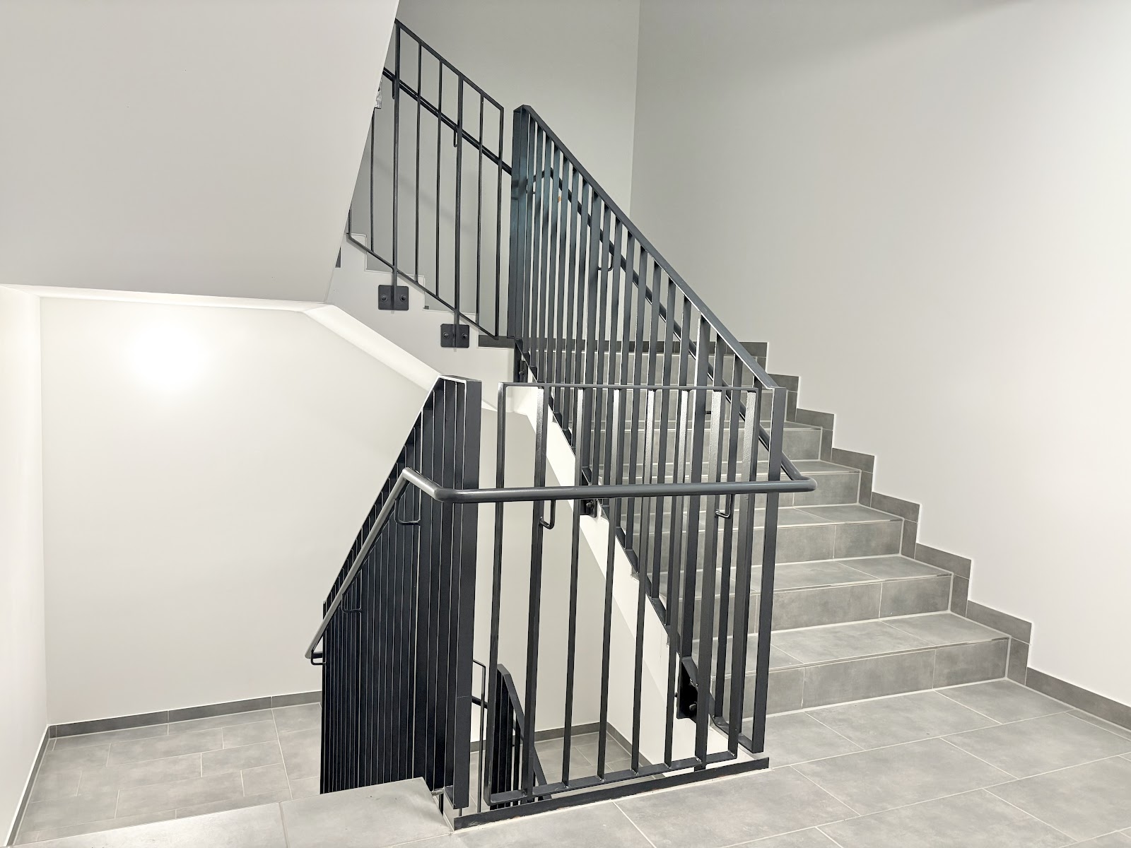 Helles Treppenhaus im Wohnhaus mit breiten Stufen, Geländern und Handläufen.