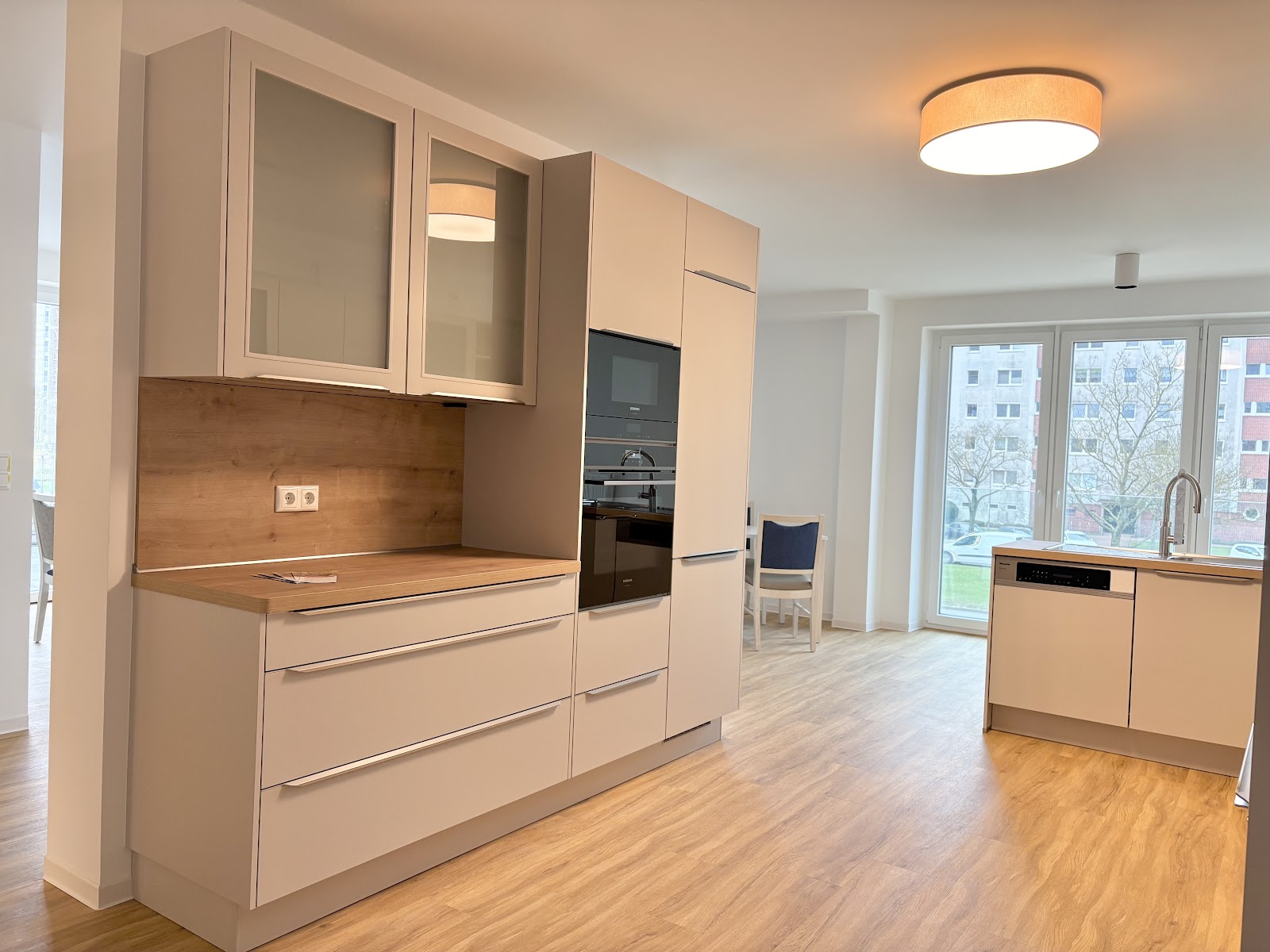 Moderne Gemeinschaftsküche mit langen Küchenzeilen, viel Stauraum, Arbeitsflächen, Backofen, Spüle und großen Fenstern.