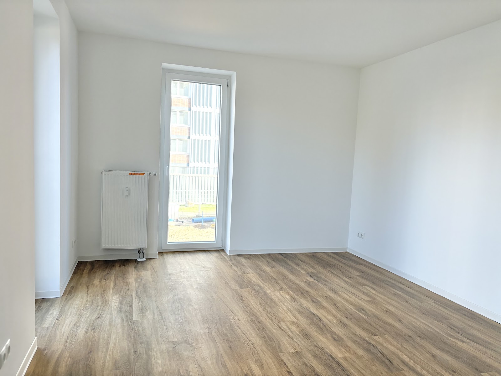 Heller Zimmerbereich mit Holzfußboden, zwei bodentiefen Fenstern, Heizkörper und viel freier Wandfläche für eigene Möbel.